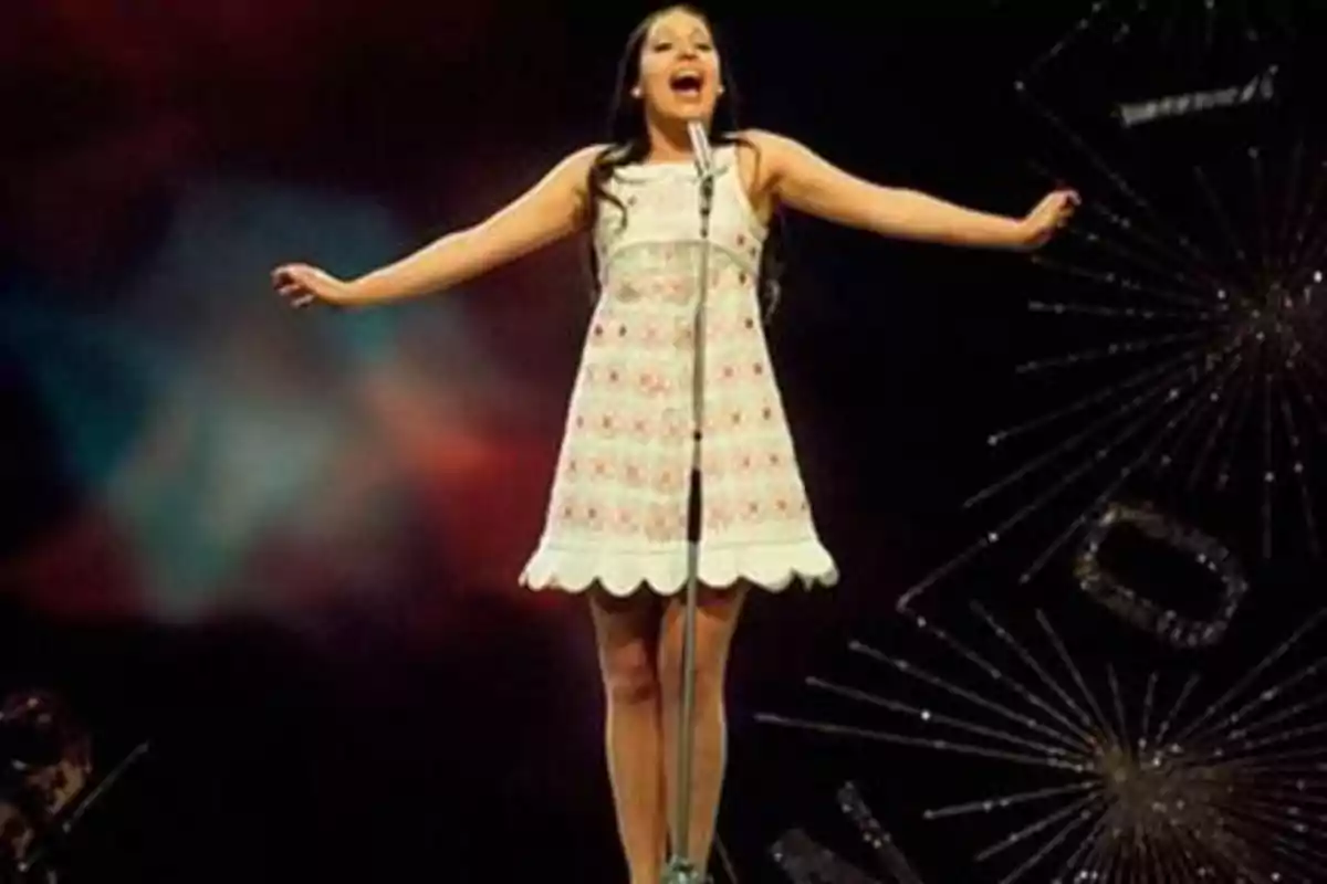 Una mujer cantando en un escenario con un vestido blanco y colorido.