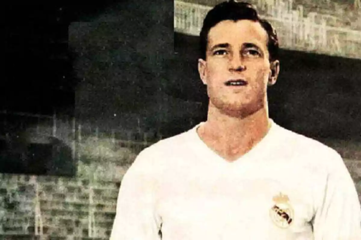 Un jugador de fútbol con una camiseta blanca y un escudo en el pecho, posando en un estadio.