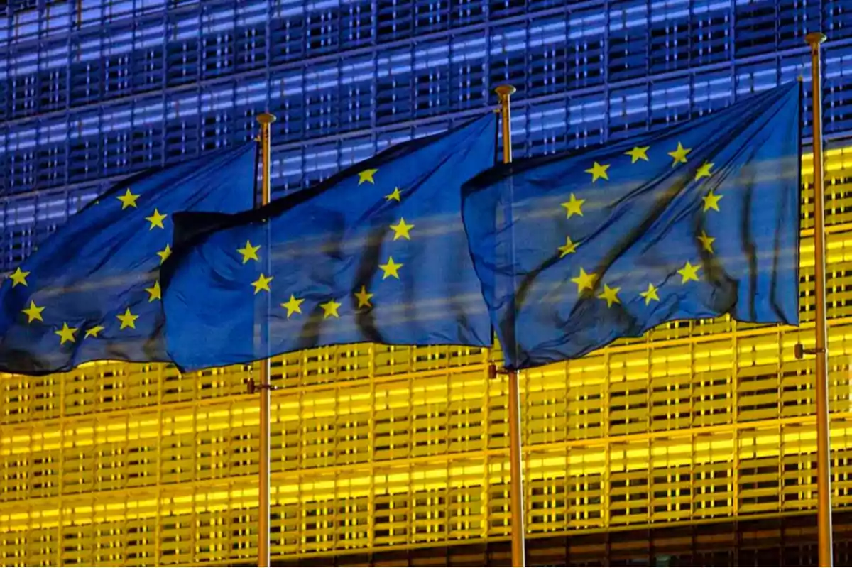 Banderas de la Unión Europea ondeando frente a un edificio iluminado.