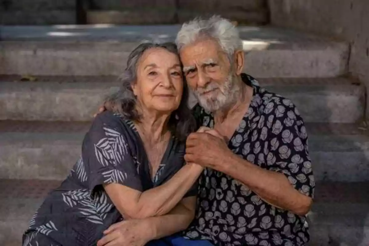Una pareja de ancianos sentados en unos escalones, abrazándose y sonriendo.
