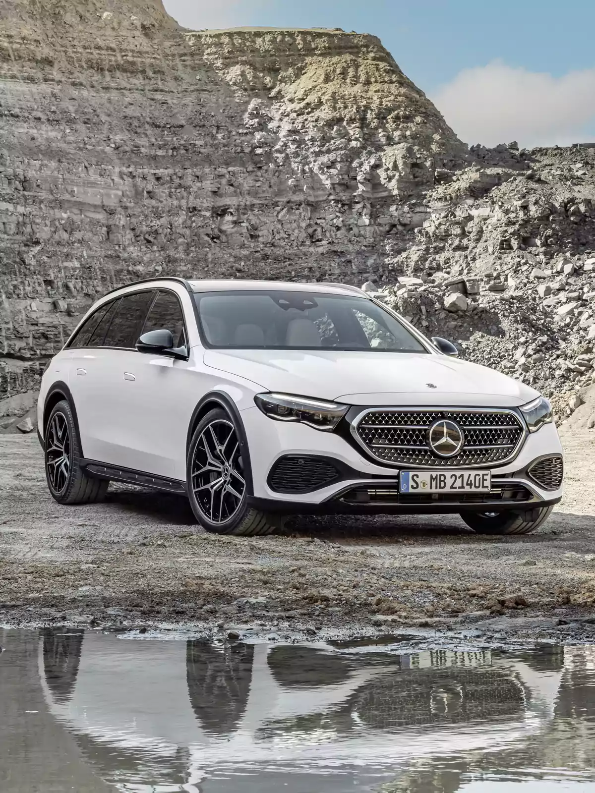 Un Mercedes-Benz E 300 de 4MATIC All-Terrain blanco de lujo estacionado en un terreno rocoso con un charco reflejando su imagen. Un Mercedes-Benz E 300 de 4MATIC All-Terrain blanco de lujo estacionado en un terreno rocoso con un charco reflejando su imagen.
