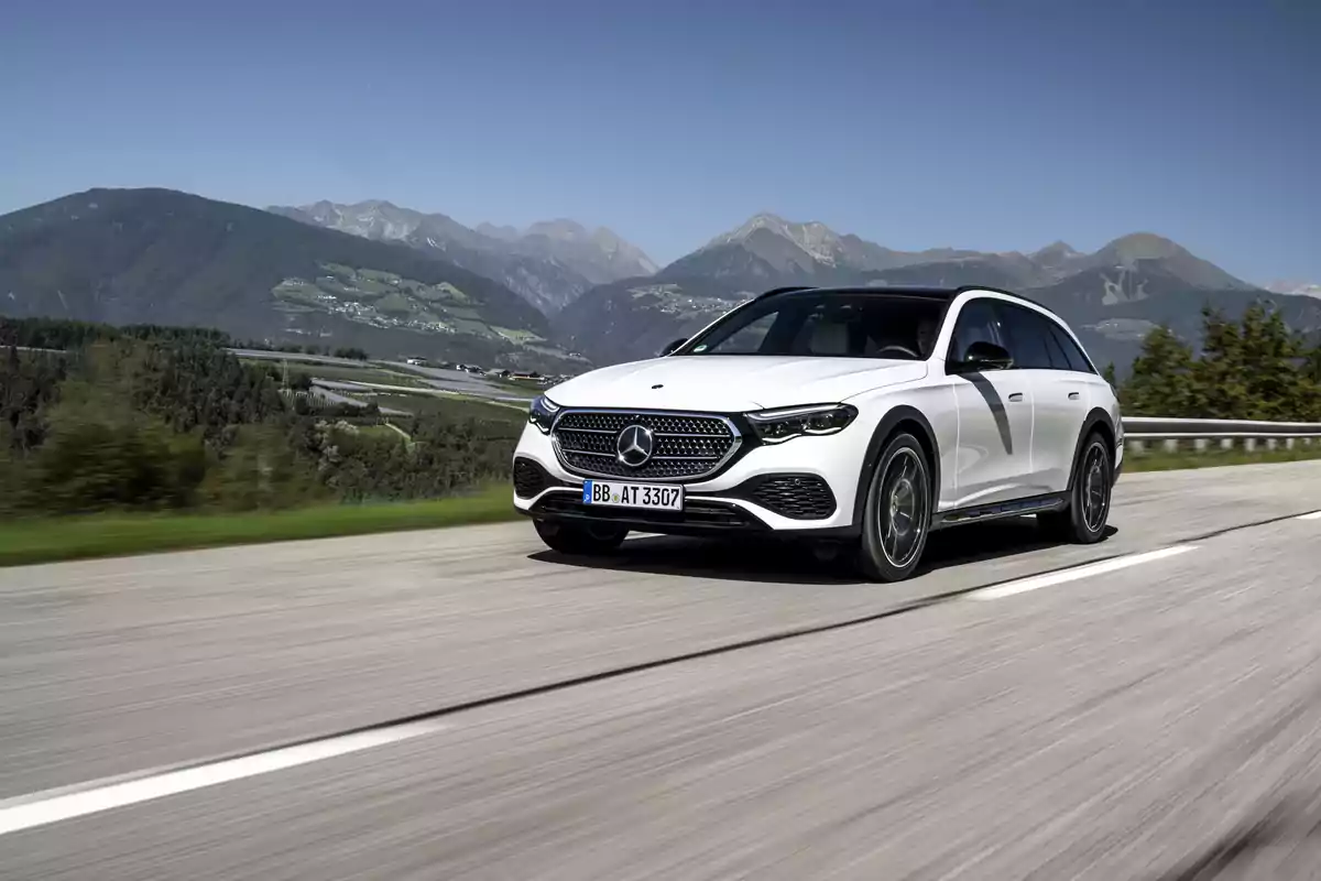 Un Mercedes-Benz E 300 de 4MATIC All-Terrain blanco de lujo circula por una carretera con un paisaje montañoso al fondo bajo un cielo despejado. Un Mercedes-Benz E 300 de 4MATIC All-Terrain blanco de lujo circula por una carretera con un paisaje montañoso al fondo bajo un cielo despejado.
