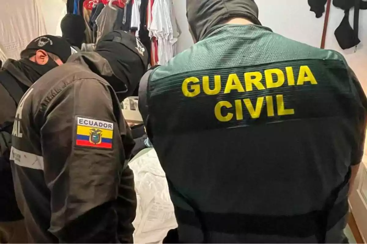 Agentes de la Guardia Civil y de Ecuador en una operación conjunta dentro de una habitación con ropa colgada.