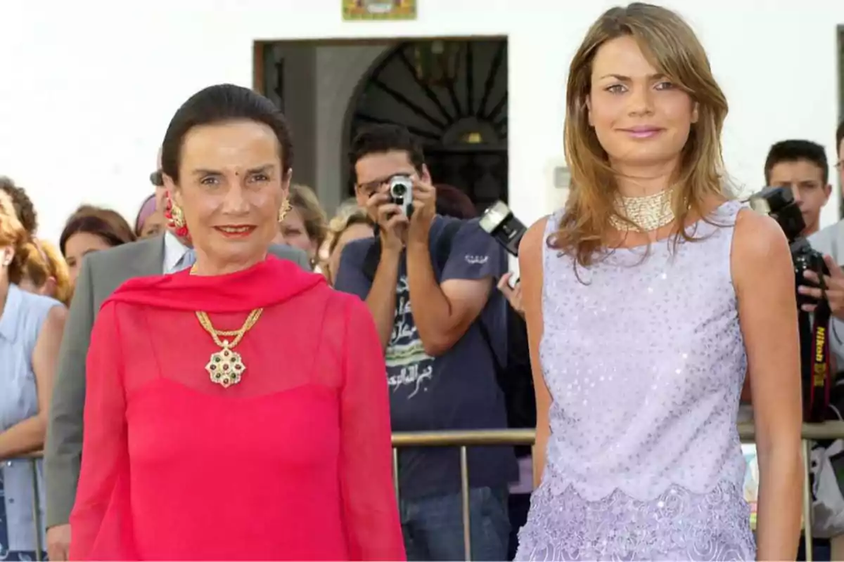 Dos mujeres posan para una foto mientras varias personas y fotógrafos están en el fondo.