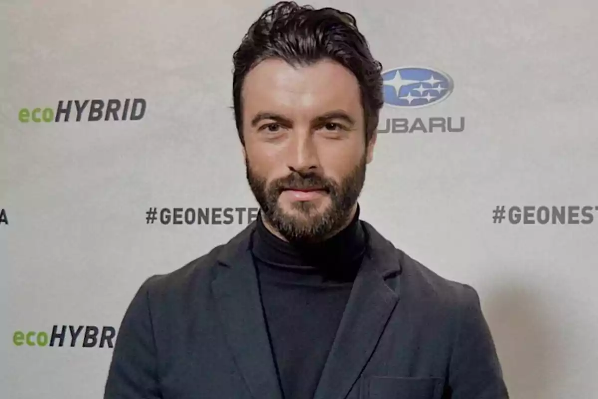 Hombre con barba y cabello oscuro en un evento de Subaru con fondo de logotipos de ecoHYBRID y #GEONESTE.