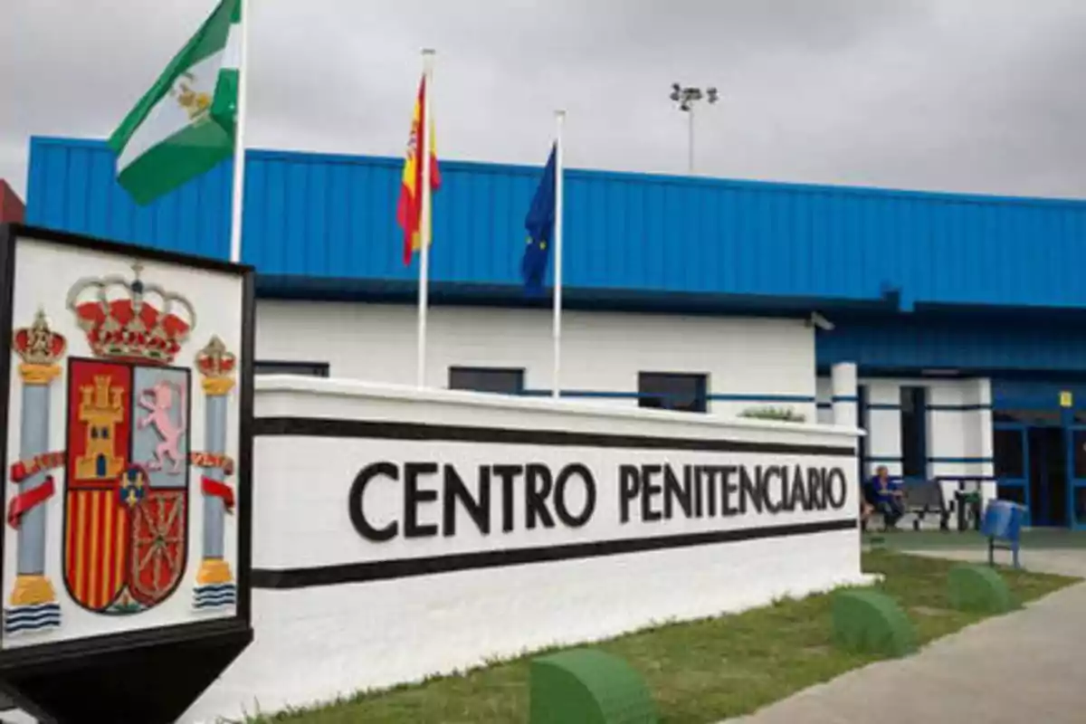 Fachada de un centro penitenciario con un escudo y tres banderas ondeando.