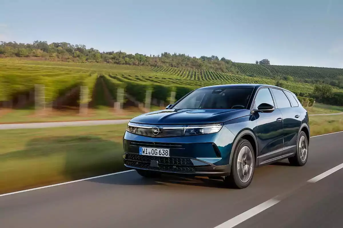 Un SUV Opel Grandland Hybrid azul oscuro circula por una carretera con un paisaje de viñedos al fondo.