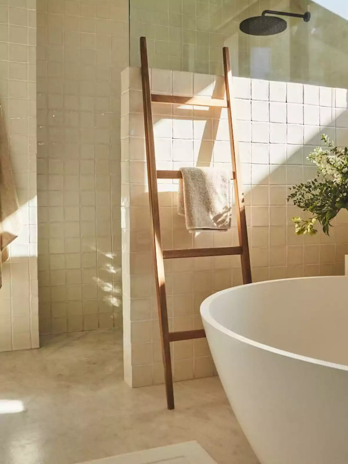 Baño moderno con una bañera blanca, una escalera de madera usada como toallero y una ducha con azulejos beige.