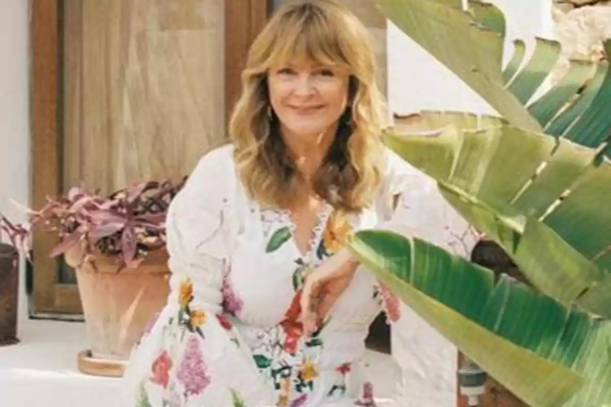 Una mujer con vestido floral posando junto a una planta en un entorno exterior.