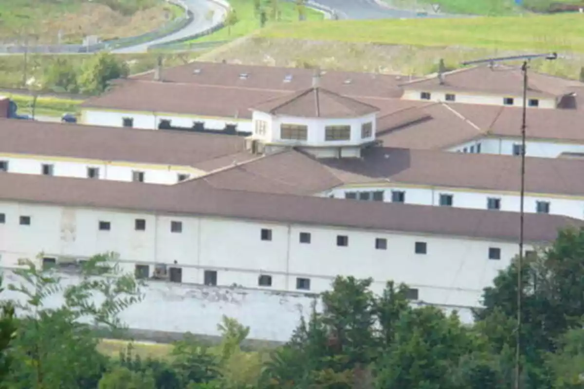 Edificio grande con techo marrón y paredes blancas rodeado de vegetación y caminos.