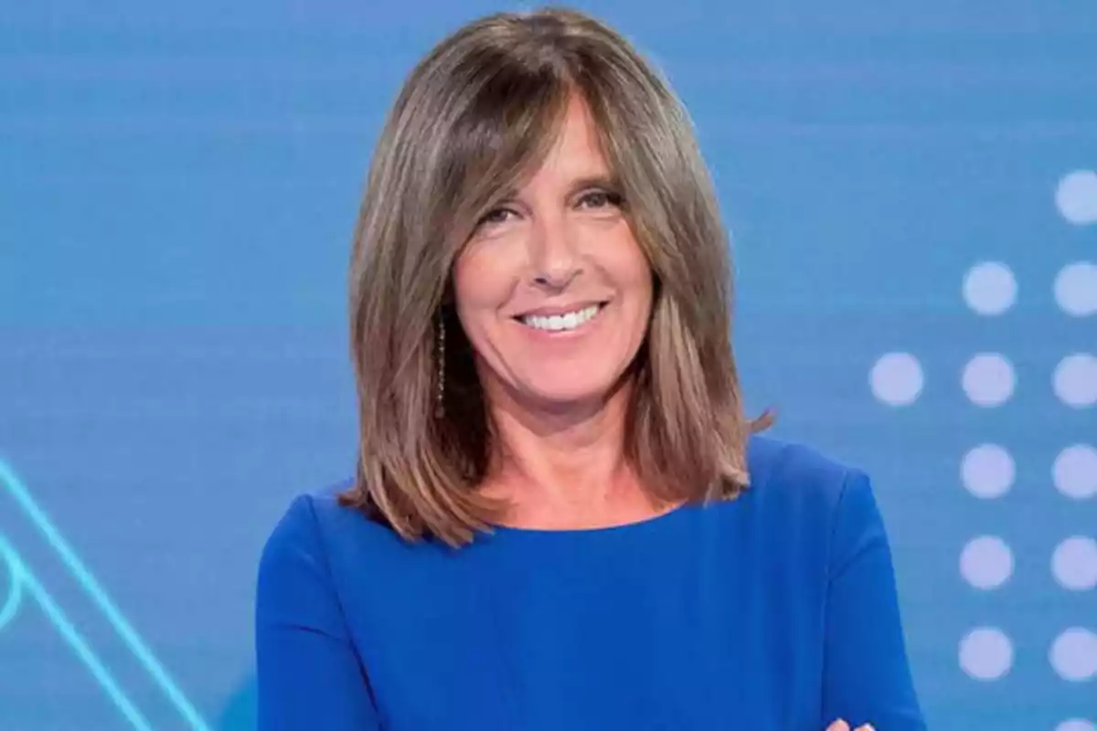 Mujer sonriendo con cabello castaño y vestido azul frente a un fondo azul con puntos blancos.