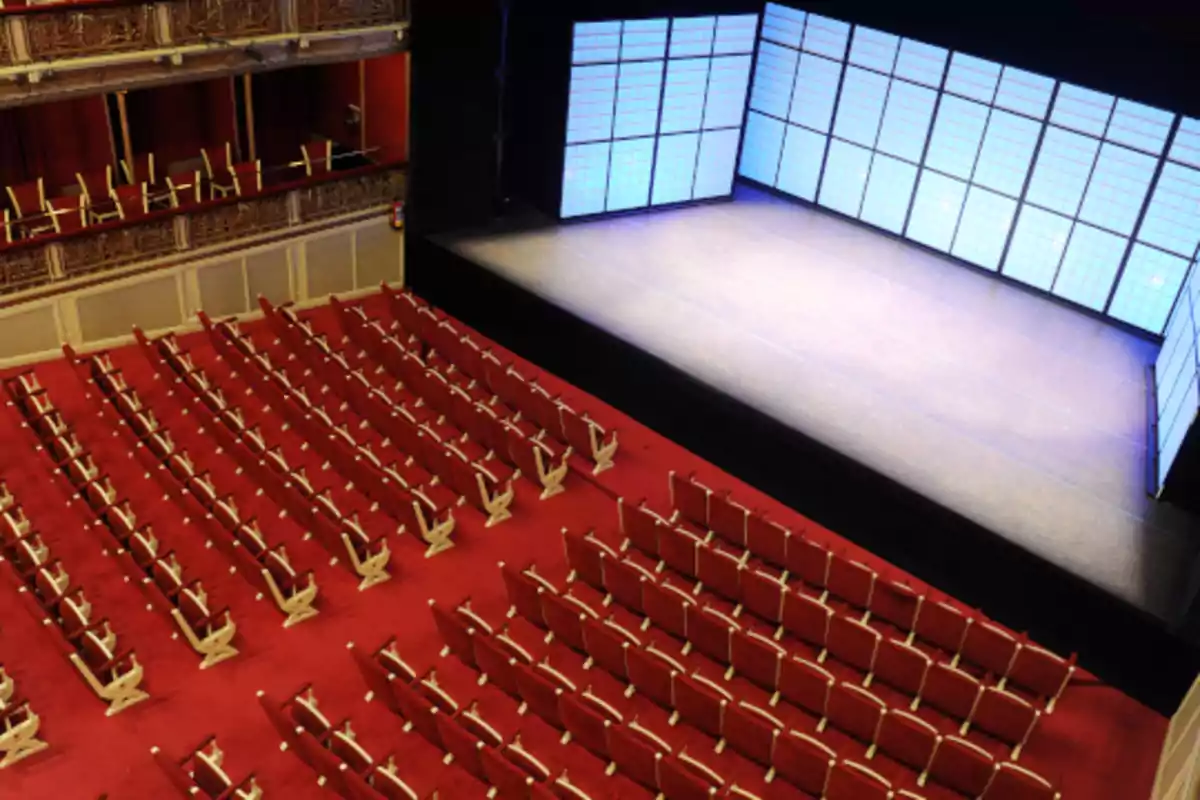Una sala de teatro con asientos rojos y un escenario iluminado con paneles de luz azul.
