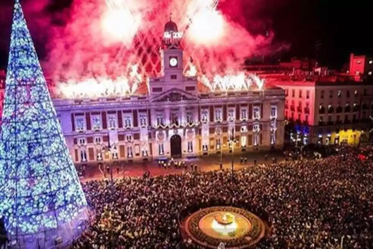 Una multitud celebra el Año Nuevo en la Puerta del Sol en Madrid, España, con un gran árbol de Navidad iluminado y fuegos artificiales sobre el edificio del reloj.