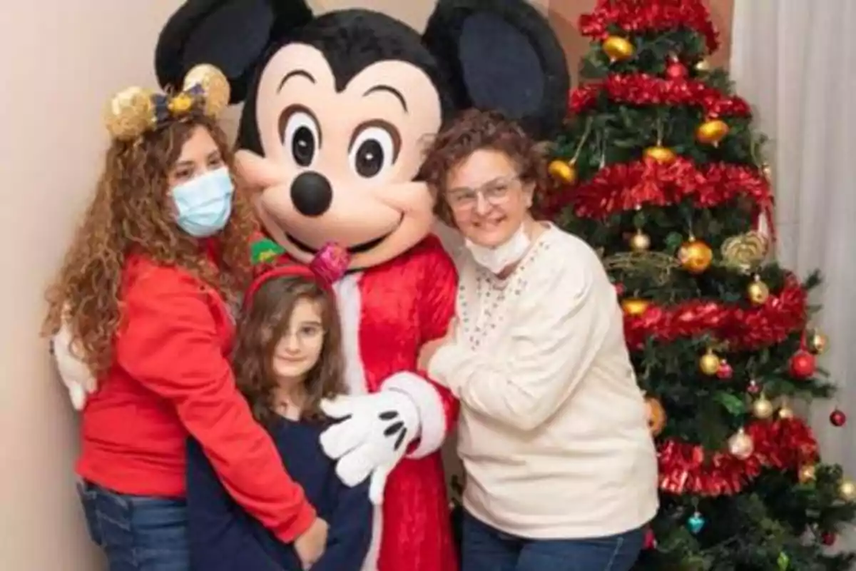 Una familia posa junto a un personaje disfrazado de Mickey Mouse frente a un árbol de Navidad decorado.