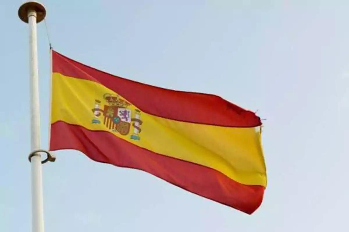 Bandera de España ondeando en un mástil contra un cielo despejado.