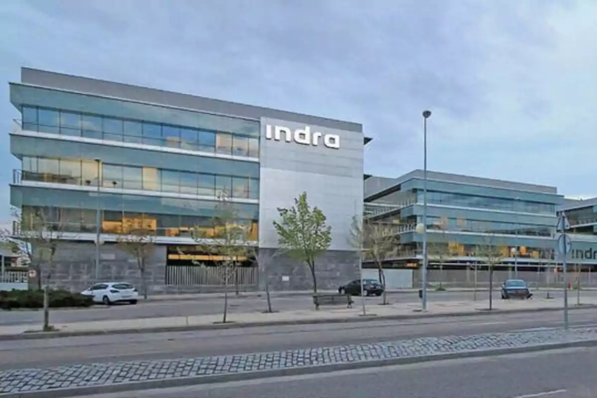 Edificio de oficinas de Indra con fachada de vidrio y metal en una calle urbana.