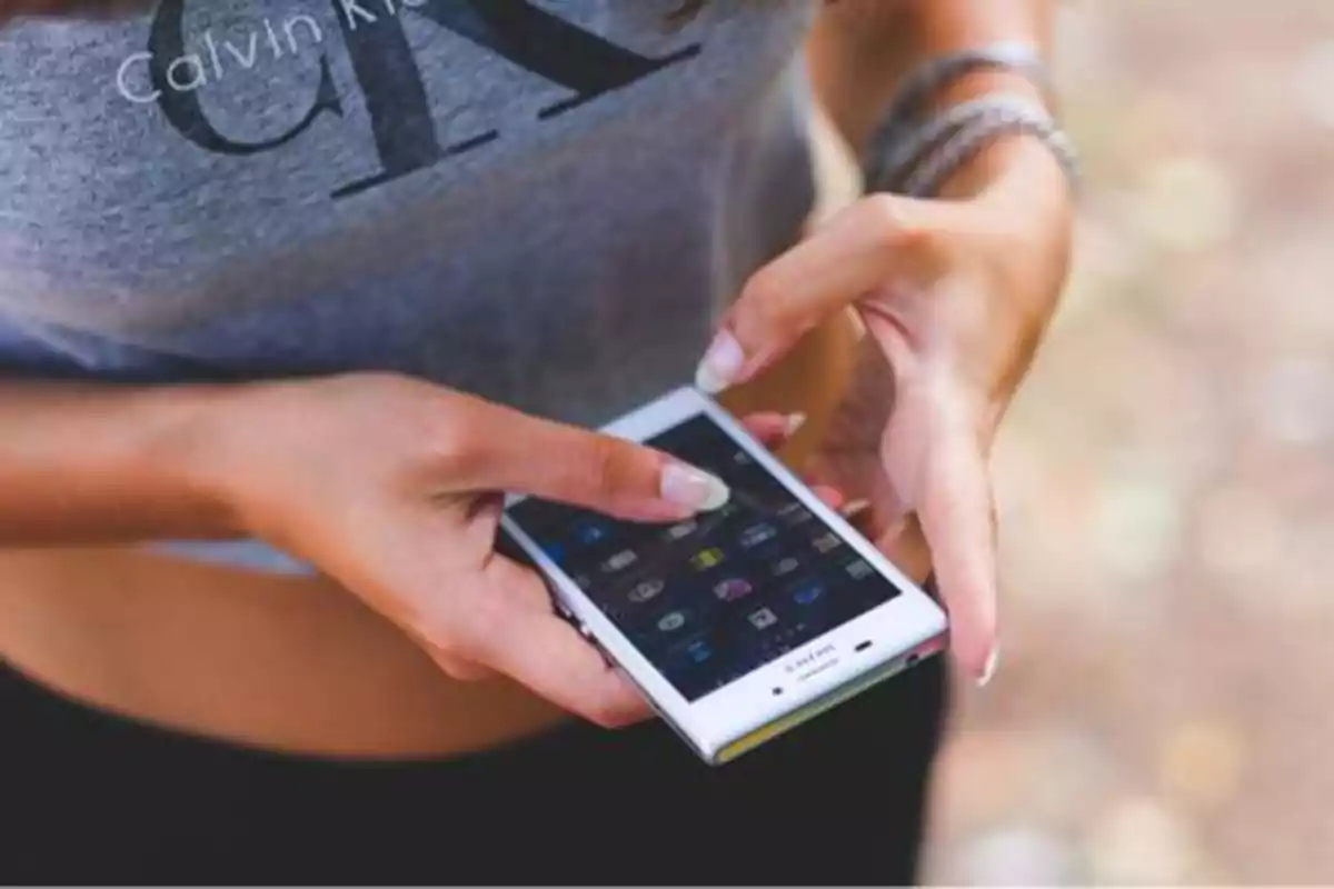 Persona usando un teléfono móvil con una camiseta gris de Calvin Klein.