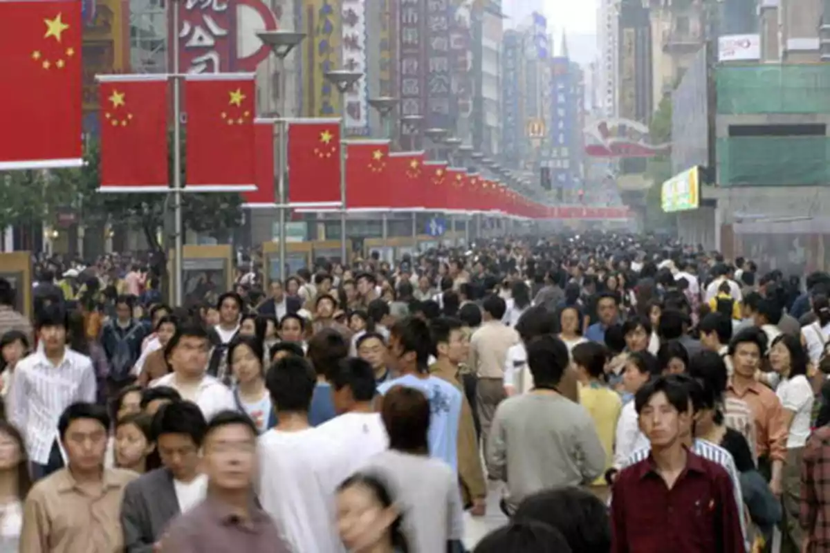 Una multitud de personas caminando por una calle comercial en China, con banderas chinas colgadas a lo largo de la vía.
