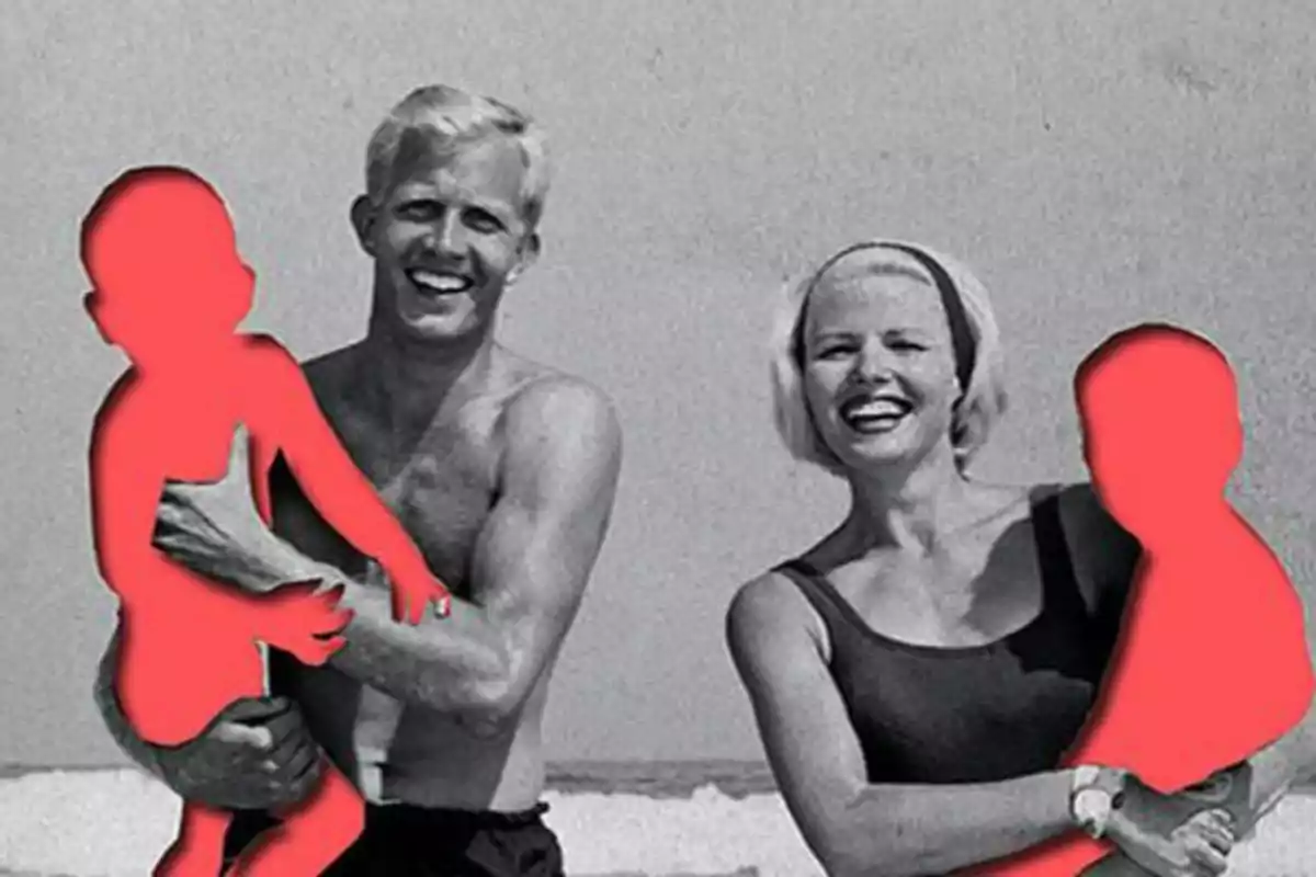 Una pareja sonriente en la playa sosteniendo siluetas rojas de niños.