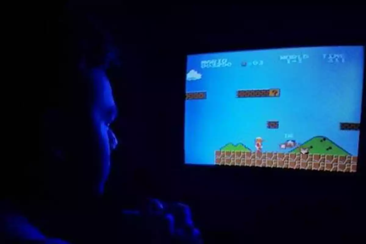 Persona jugando un videojuego retro en una pantalla iluminada en una habitación oscura.