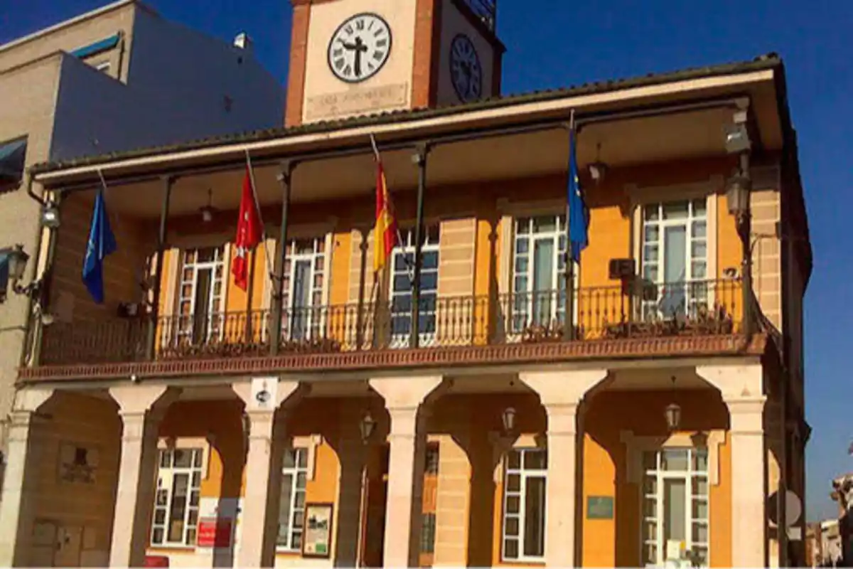Edificio de dos pisos con reloj en la parte superior y varias banderas en el balcón.
