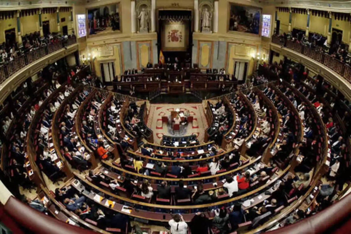 Vista panorámica del interior de un parlamento con numerosos asientos ocupados por personas.