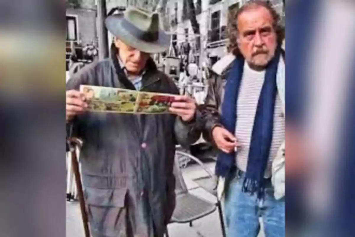 Dos hombres están de pie en una calle, uno de ellos sostiene un cómic mientras el otro mira hacia la cámara.