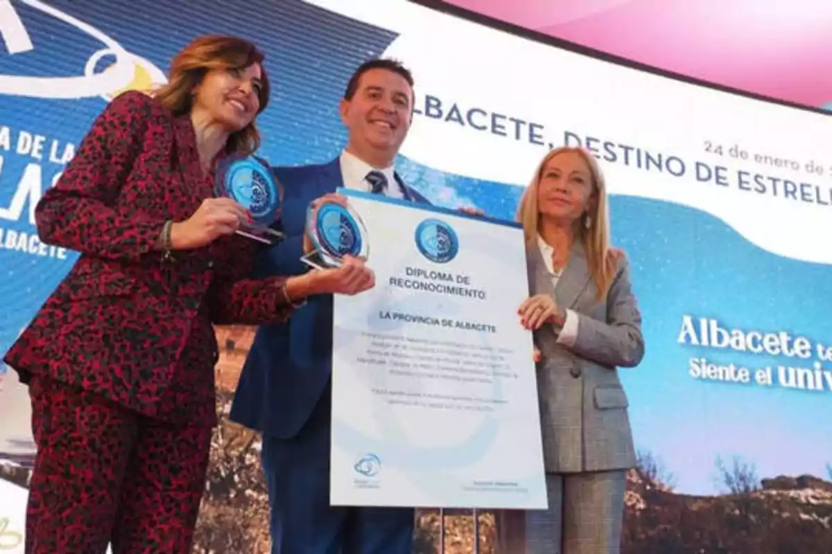 Tres personas posan con un diploma de reconocimiento y trofeos en un evento en Albacete.