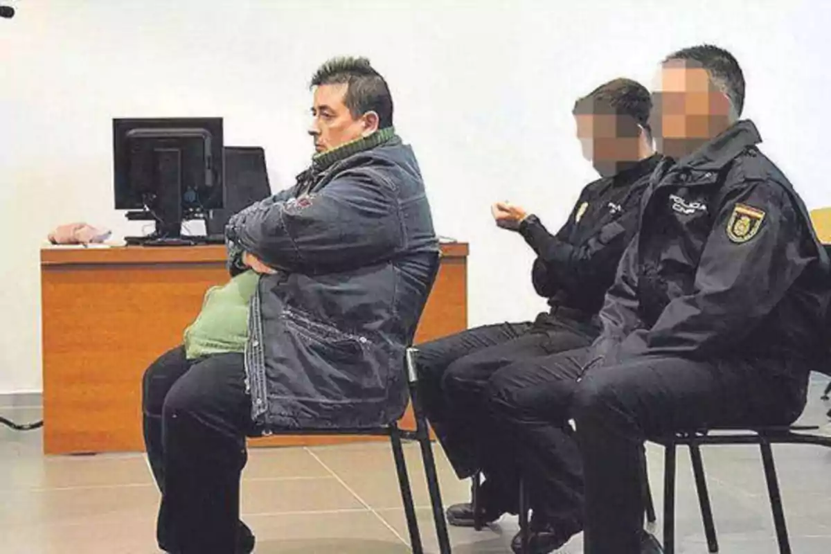 Una persona sentada en una sala junto a dos policías con rostros pixelados.