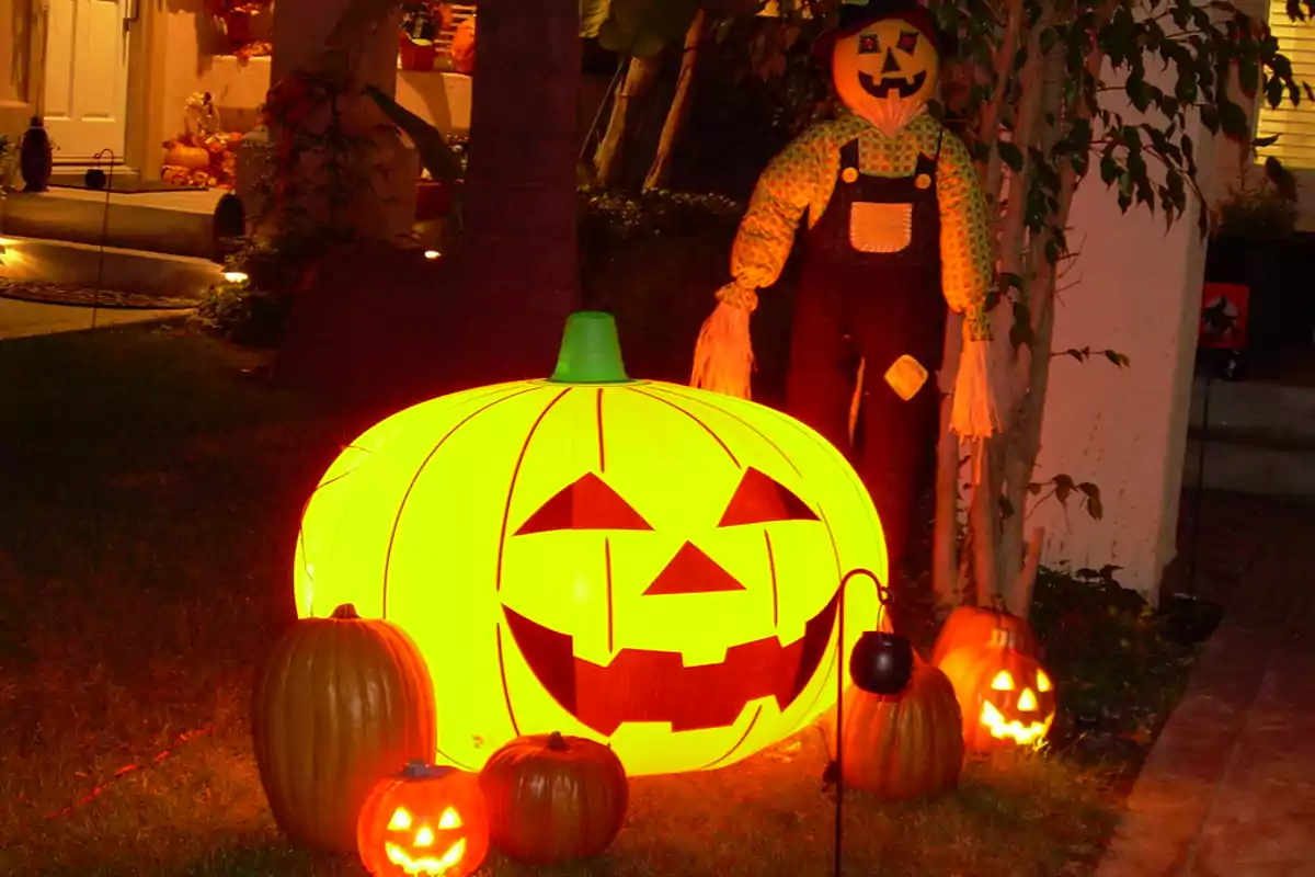 Decoración de Halloween con una calabaza iluminada y un espantapájaros en un jardín.