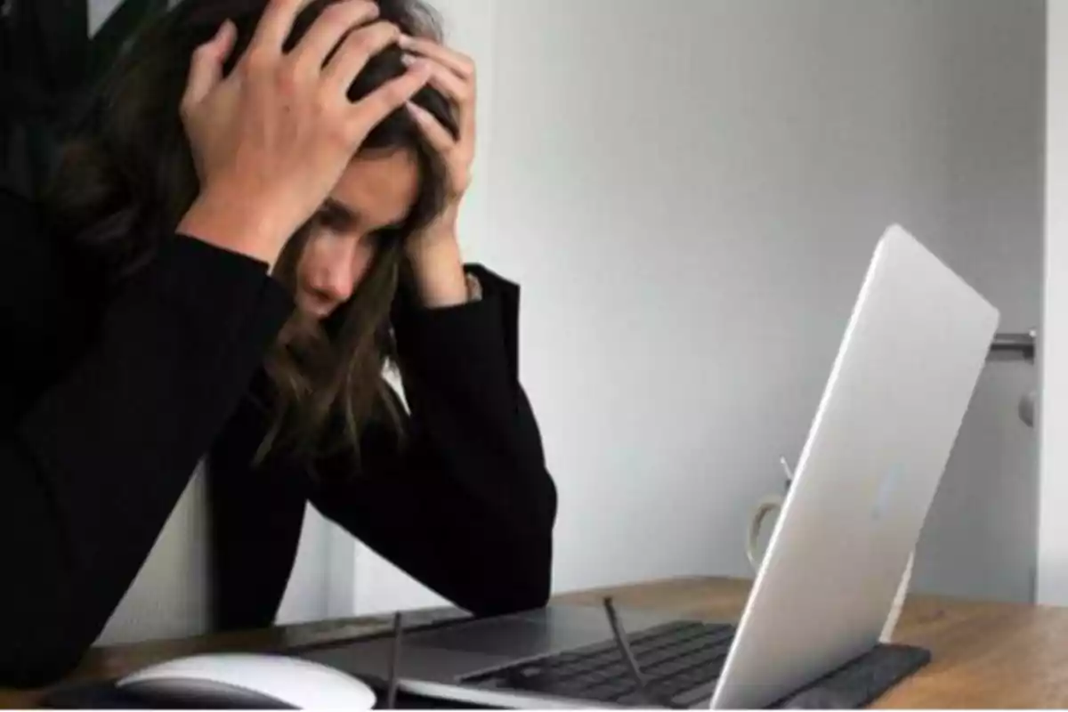 Persona con las manos en la cabeza frente a una computadora portátil, mostrando signos de estrés o frustración.