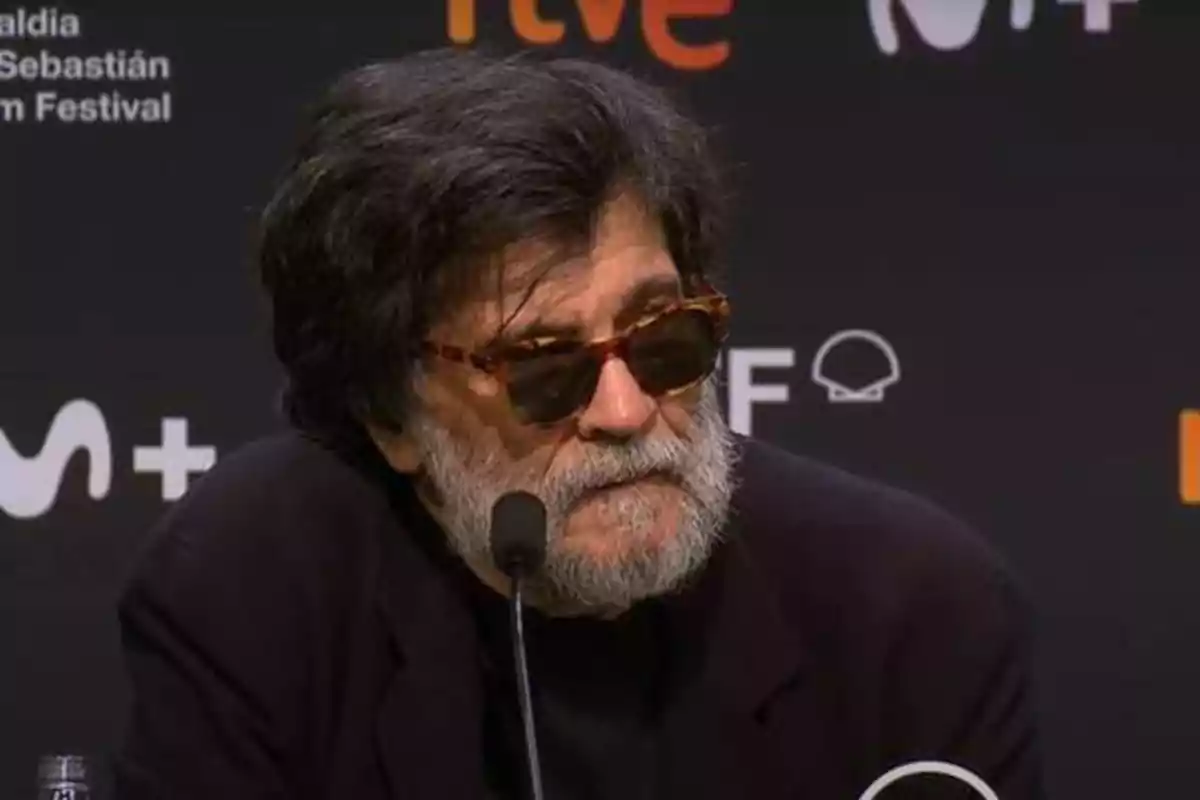 Un hombre con barba y gafas de sol habla en una conferencia de prensa. Detrás de él, se pueden ver logotipos y texto relacionados con el Festival de Cine de San Sebastián.
