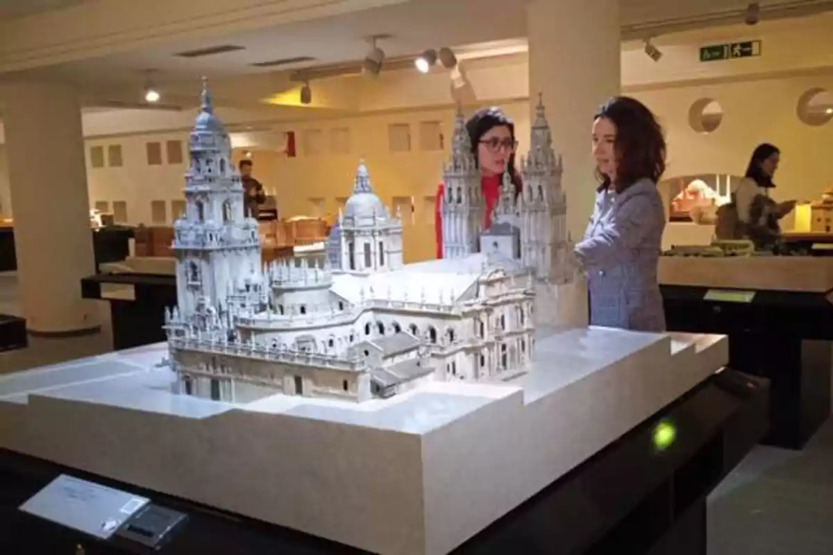 Dos mujeres observan una maqueta detallada de una catedral en una exposición.