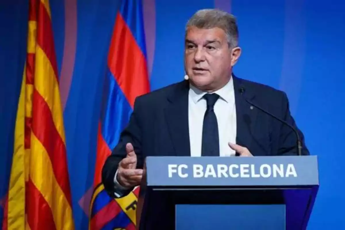 Hombre de traje y corbata hablando en un podio con el texto "FC BARCELONA" y banderas en el fondo.