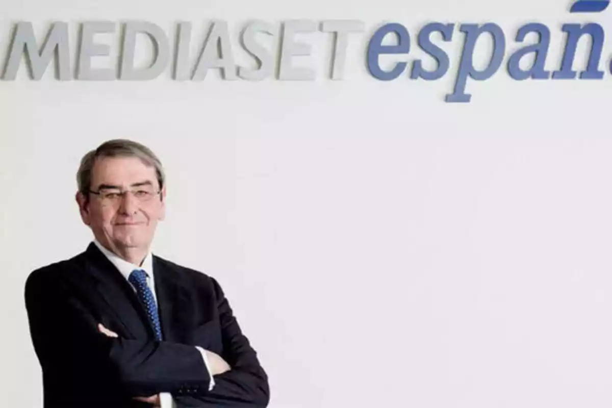 Hombre de traje y corbata con los brazos cruzados frente a un cartel de Mediaset España.