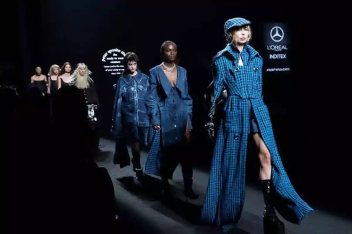 Desfile de moda con modelos vistiendo prendas de diseñador en tonos azules sobre una pasarela iluminada.