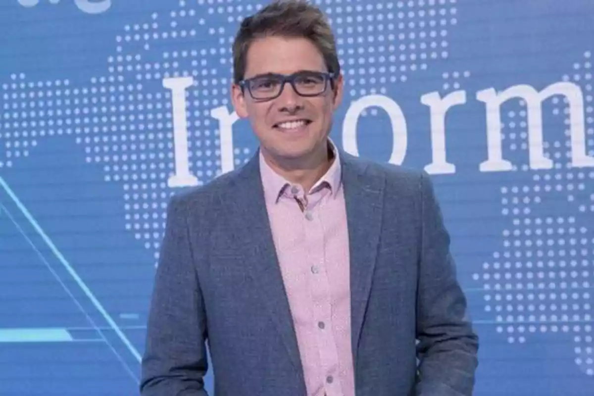 Hombre con gafas y traje gris sonriendo frente a un fondo azul con texto.