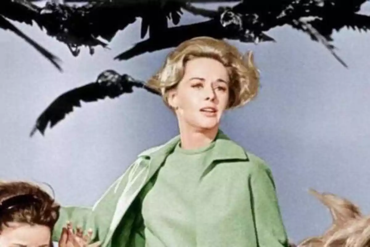 Una mujer con abrigo verde parece asustada mientras varios pájaros negros vuelan sobre ella.