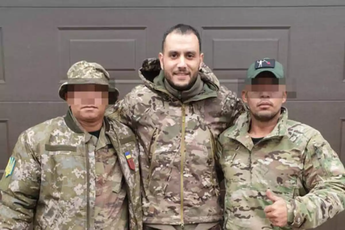 Tres hombres con ropa de camuflaje militar posan juntos frente a una puerta.