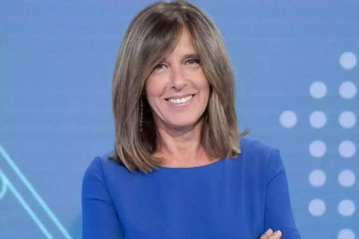 Mujer sonriendo con cabello castaño y vestido azul frente a un fondo azul con puntos blancos.