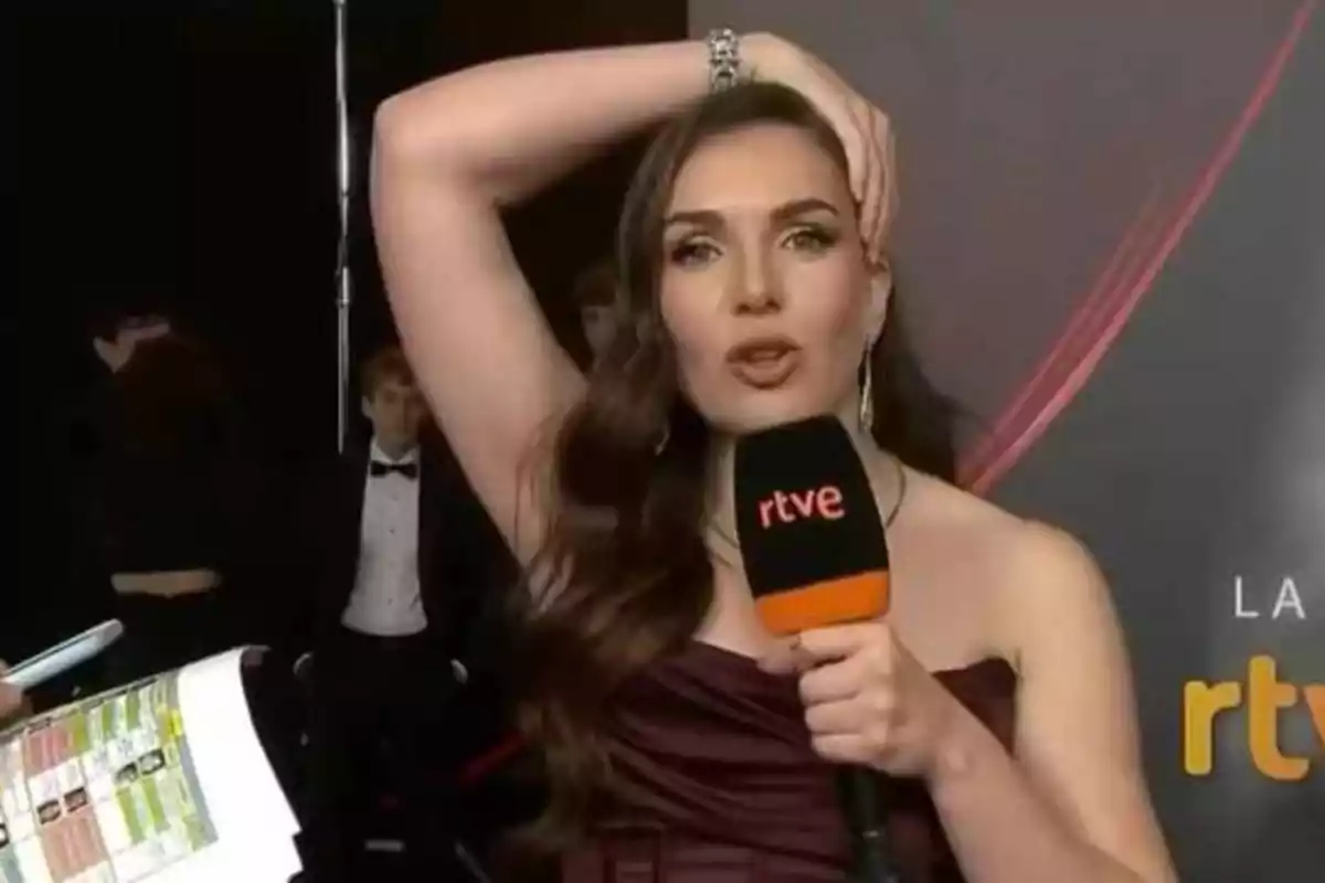 Mujer con vestido elegante sosteniendo un micrófono de RTVE en un evento.