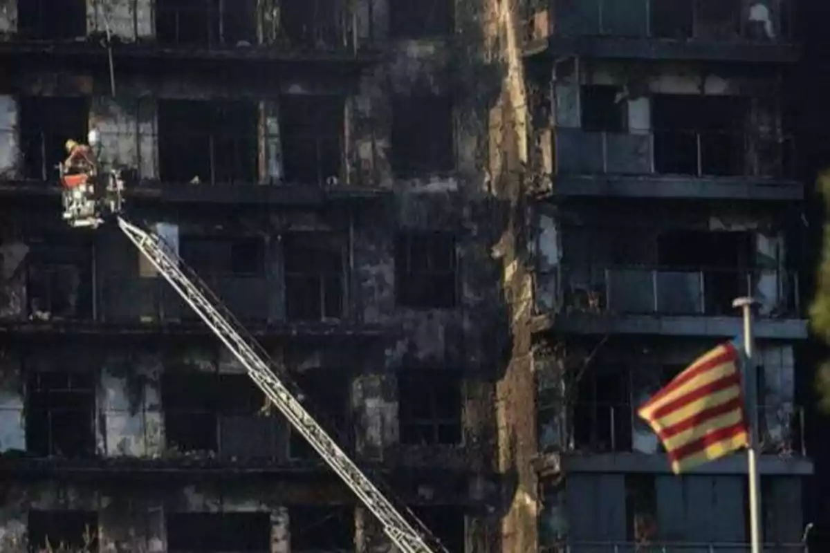 Un edificio quemado con un bombero en una escalera y una bandera ondeando en primer plano.