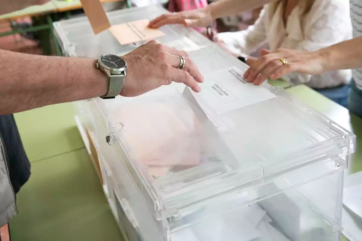 Personas depositando votos en una urna transparente durante una elección.