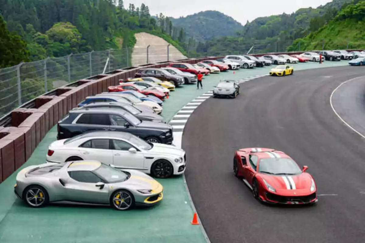 Una fila de autos estacionados junto a una pista de carreras en un entorno montañoso.