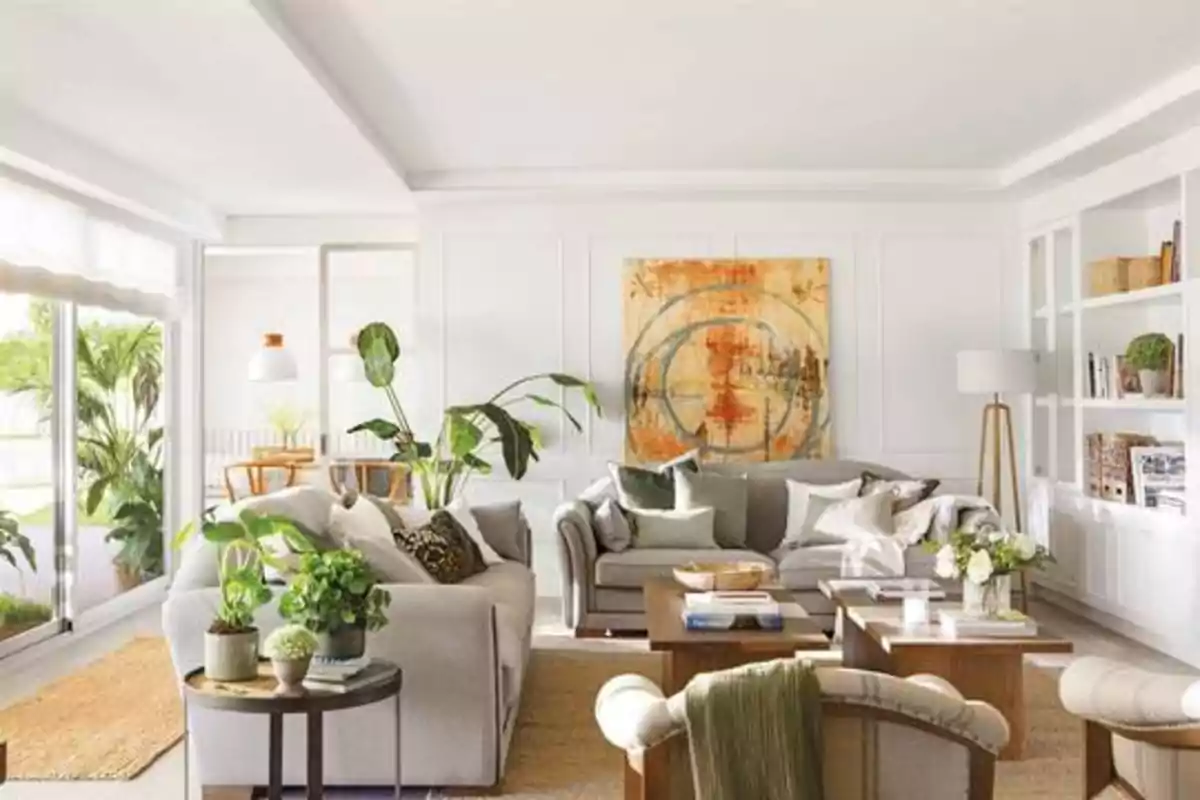 Sala de estar moderna y luminosa con sofás grises, plantas decorativas, una mesa de centro de madera y una pintura abstracta en la pared.