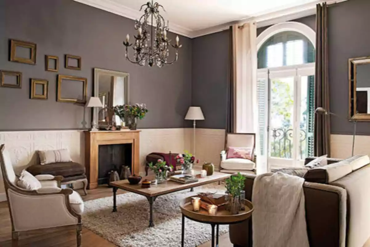 Sala de estar elegante con paredes grises, chimenea, candelabro, muebles clásicos y grandes ventanales.