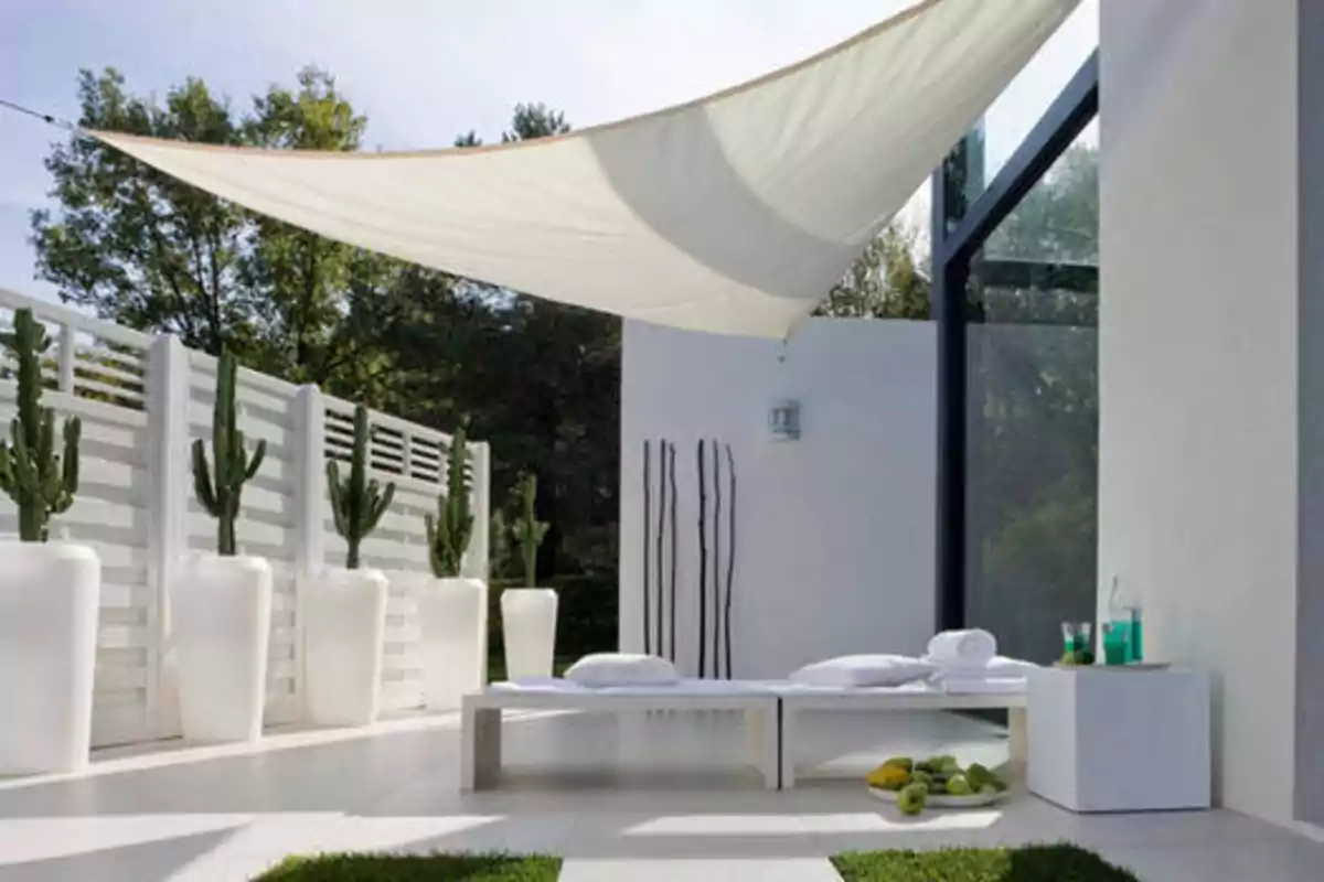 Terraza moderna con tumbonas blancas, toldo de tela, macetas grandes con cactus y mesa auxiliar con bebidas.