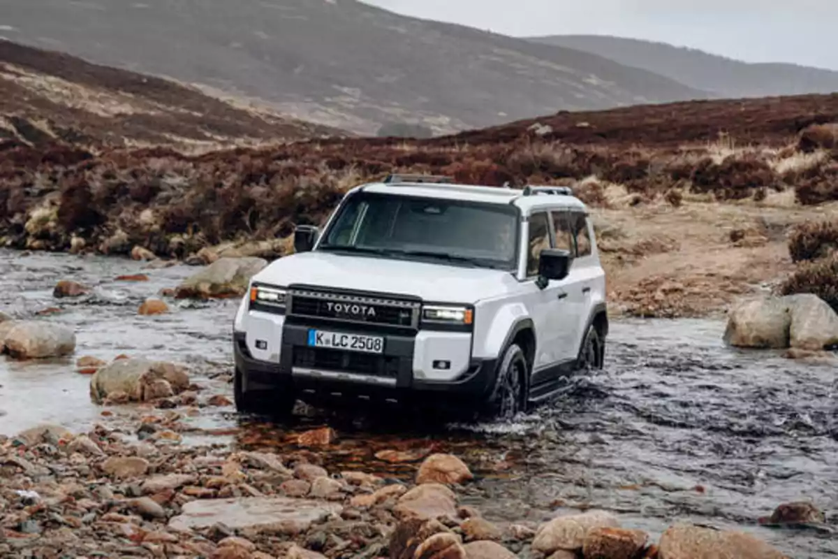 Un Toyota Land Cruiser blanco cruzando un arroyo en un paisaje montañoso.