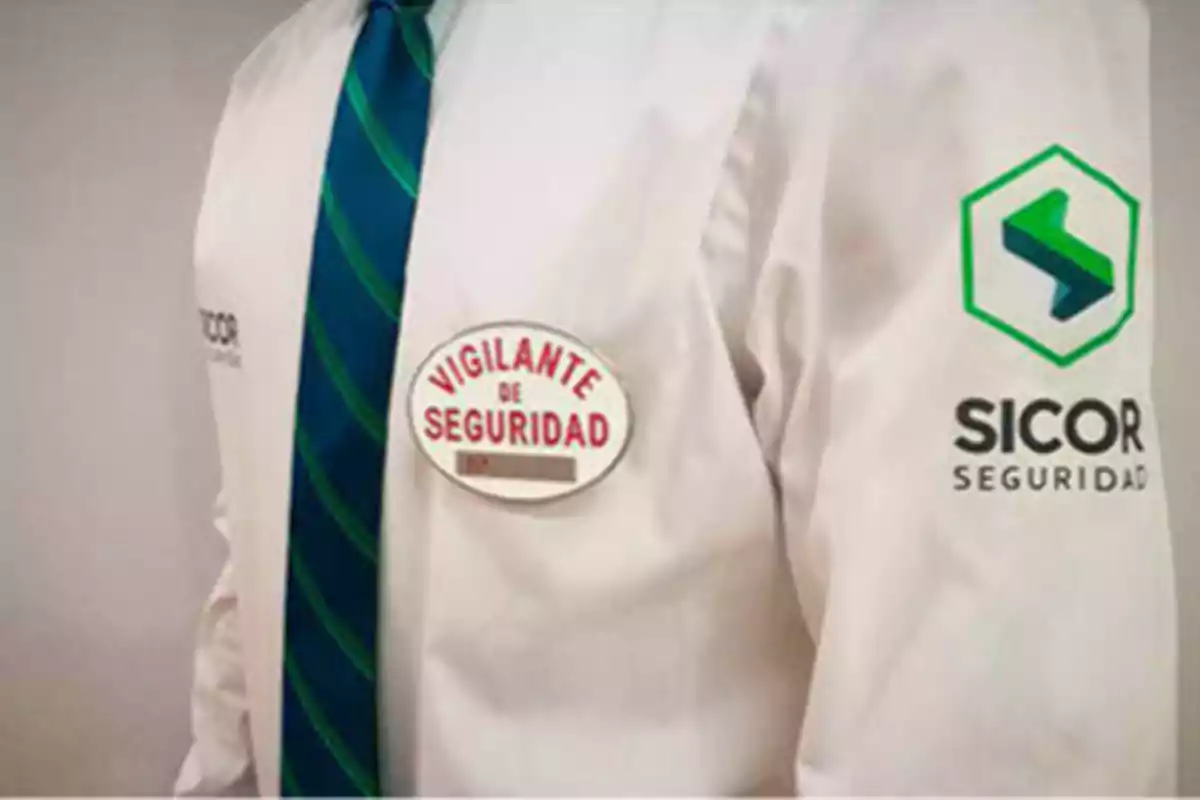 Un vigilante de seguridad con uniforme de SICOR Seguridad, que incluye una camisa blanca, una corbata verde con rayas azules y un distintivo en el pecho que dice "Vigilante de Seguridad".