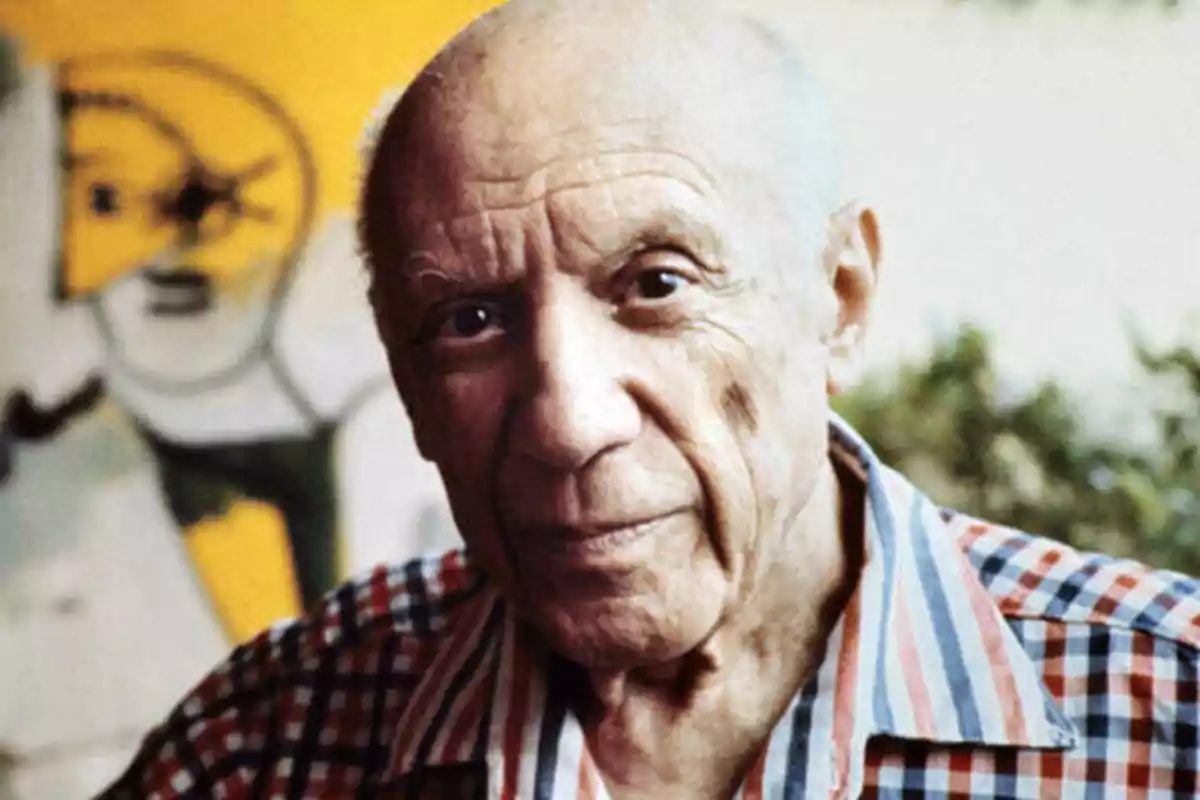 Un hombre mayor con una camisa de rayas posa frente a una pintura abstracta.